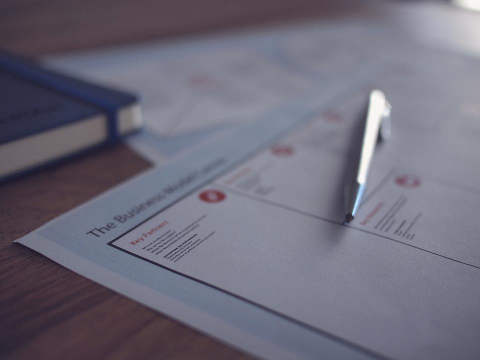 Foglio stampato su una scrivania con una penna appoggiata e un quaderno blu sullo sfondo.